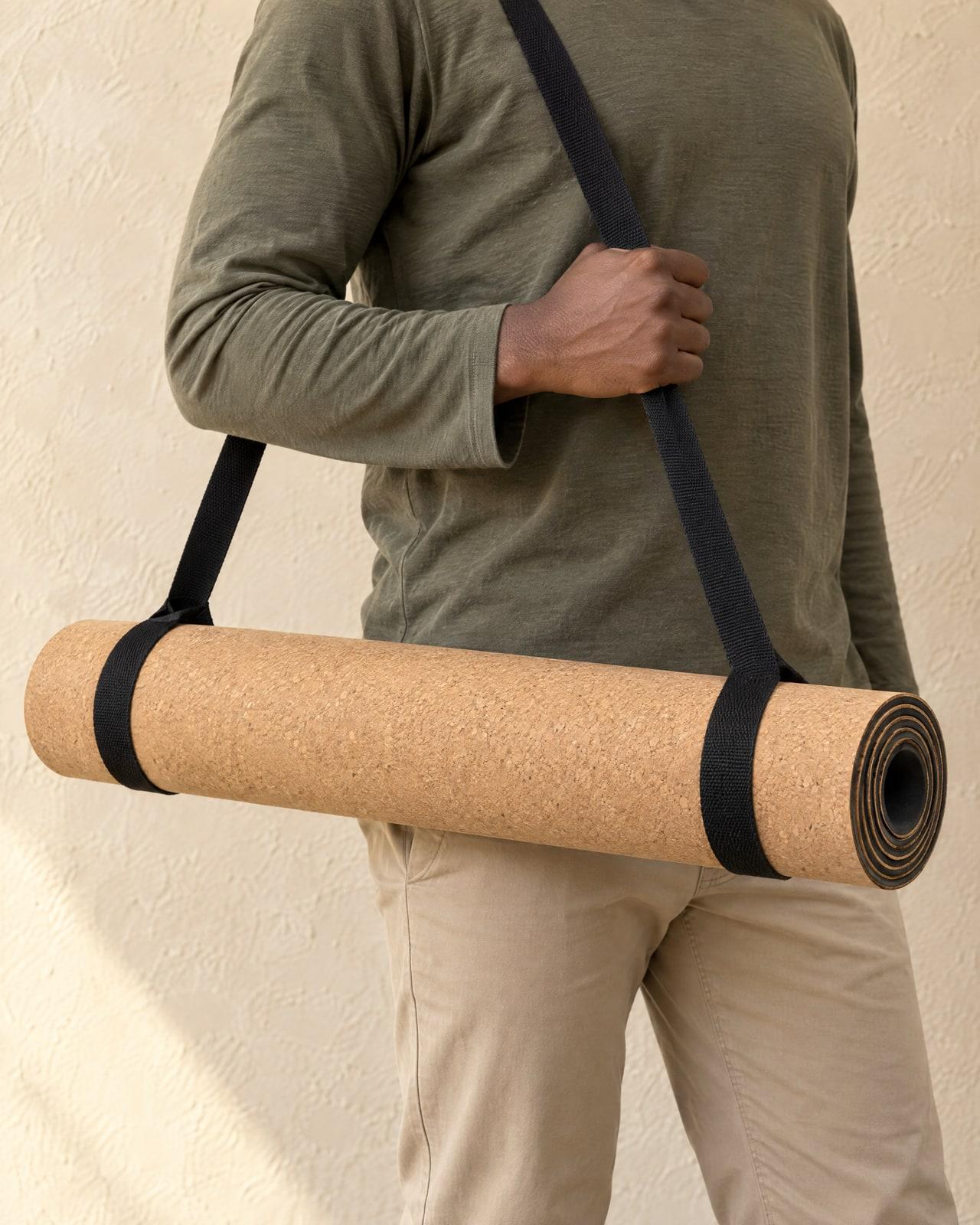 Someone in an olive top carries the rolled mat in a black carry sling, cropped at the shoulders.